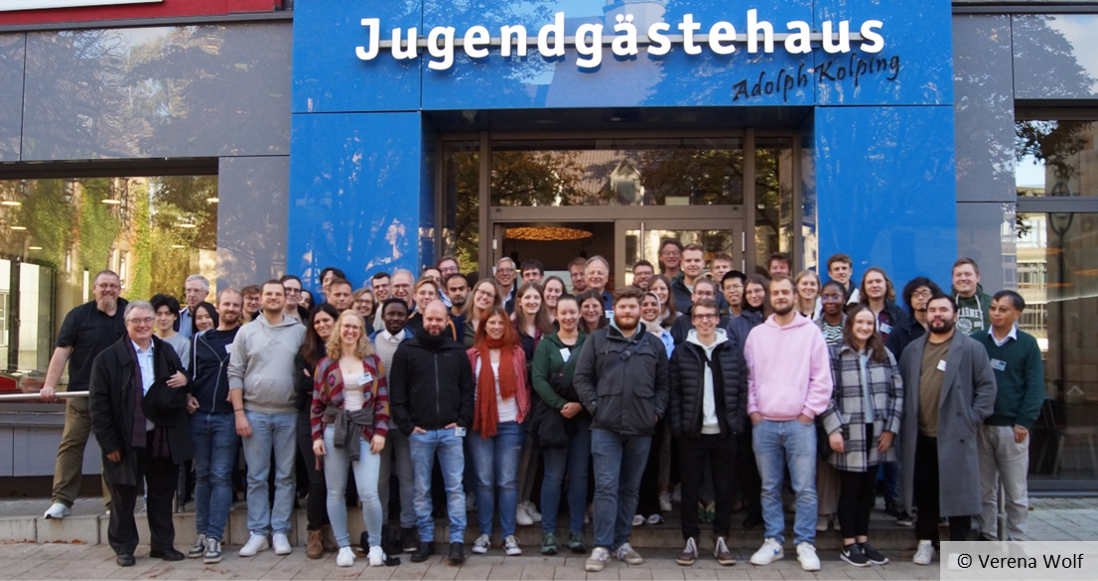 A large group of people is standing in front of a building. The words ‘Jugendgästehaus Adolph Kolping’ can be read above the entrance to the building.