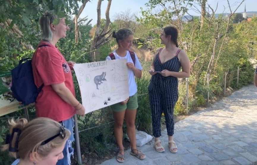 Two people are standing in the zoo holding a poster.