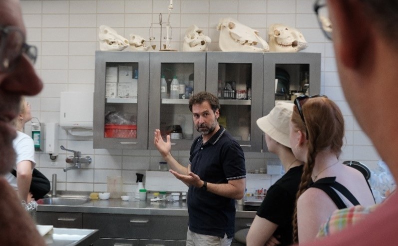 Chadi Touma stands in front of students in a laboratory and appears to be explaining something. Animal skulls can be seen in the background.