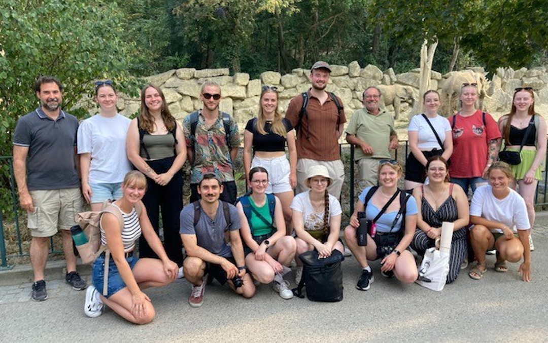 A group of people in front of an elephant enclosure smiling into the camera.