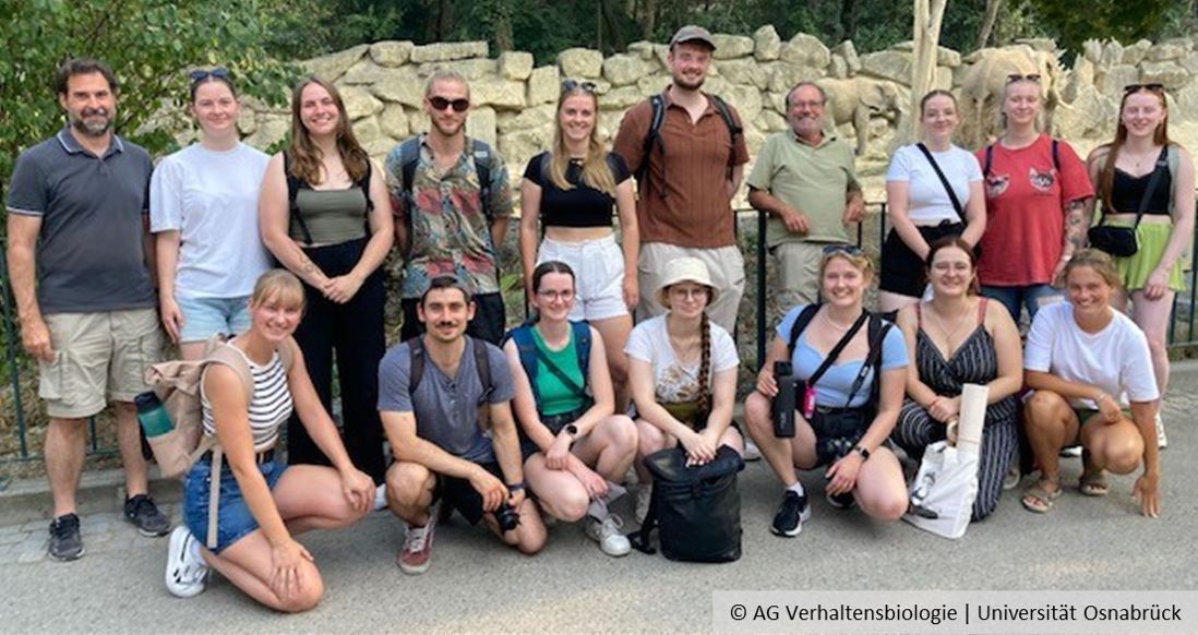 A group of people in front of an elephant enclosure smiling into the camera.